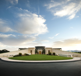 Moderne Architektur vor bewölktem Himmel, umgeben von grünem Rasen und gepflasterter Straße.